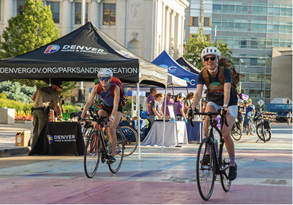 Two bicyclists riding down a street in downtown Denver, with Denver-branded canopies along the street